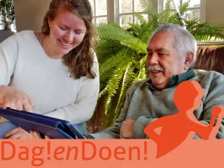 Een jongere vrouw geeft uitleg over de tablet aan een oudere meneer